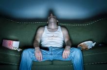 A man sleeps in upright position on his couch.